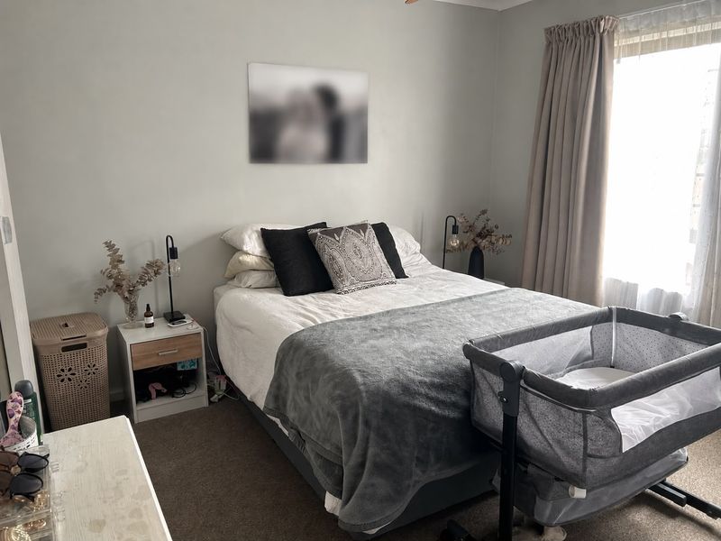 A functional bedroom featuring neutral wall tones, carpeted flooring, and natural light provided by a window with installed curtain tracks.