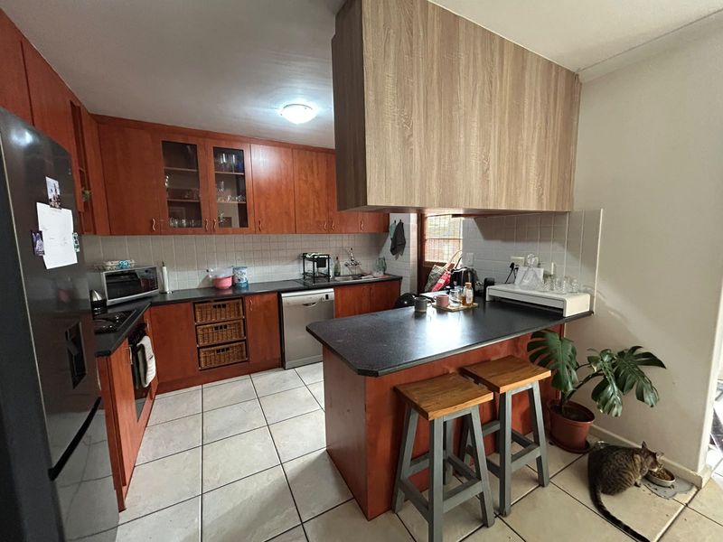 A functional kitchen featuring wood-tone cabinetry, dark countertops, a breakfast bar, and tiled flooring, offering a practical layout for daily meal preparation.