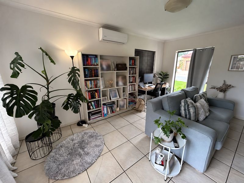 A bright living room featuring ceramic floor tiles, a wall-mounted split-system air conditioner, and a sliding glass door providing natural light.