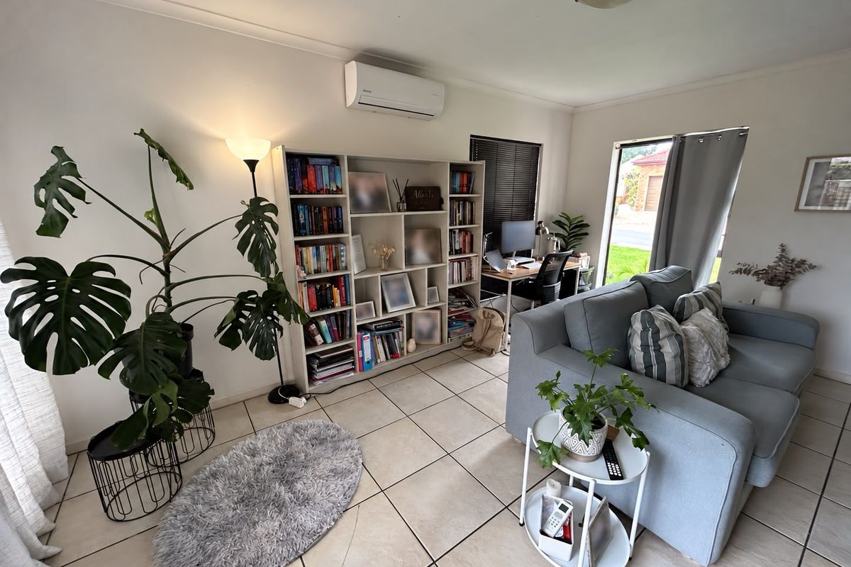 A bright living room featuring ceramic floor tiles, a wall-mounted split-system air conditioner, and a sliding glass door providing natural light.