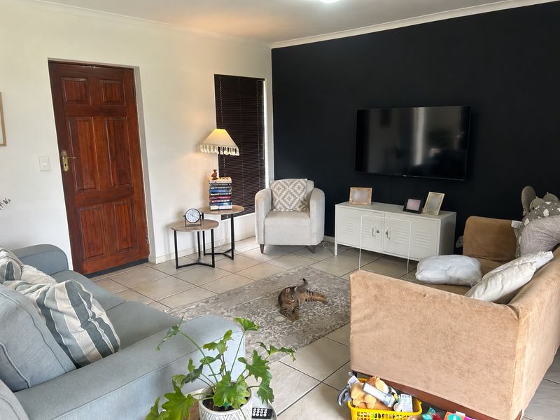 A comfortable living room featuring tiled flooring, a dark accent wall, and a timber entrance door with natural light from the window.
