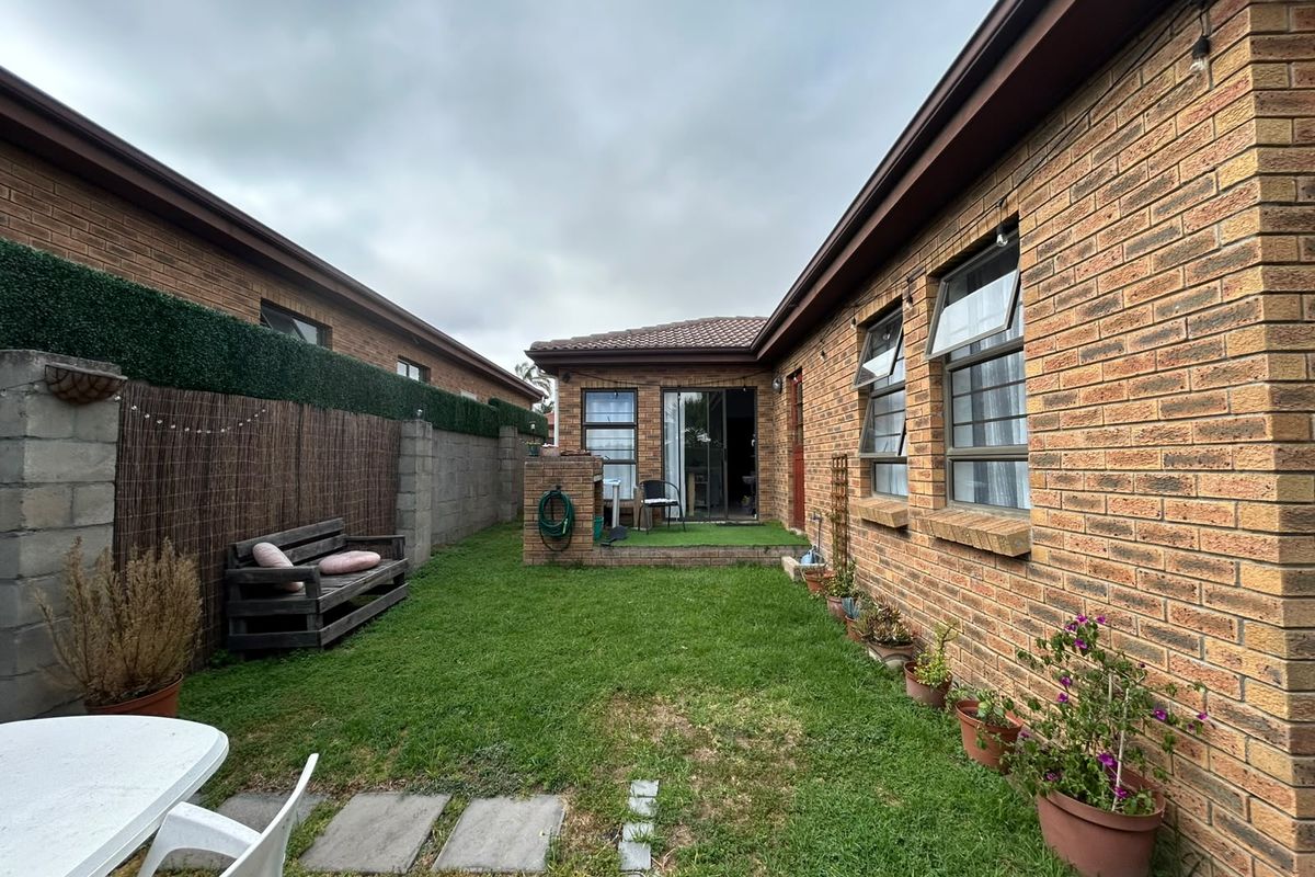 A private rear garden featuring a face brick townhouse exterior, a small paved patio, and a lawn area enclosed by boundary walls.