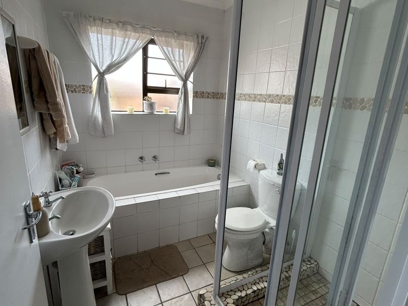 A functional bathroom featuring a pedestal basin, built-in bathtub, and a separate shower enclosure with tiled finishes throughout.