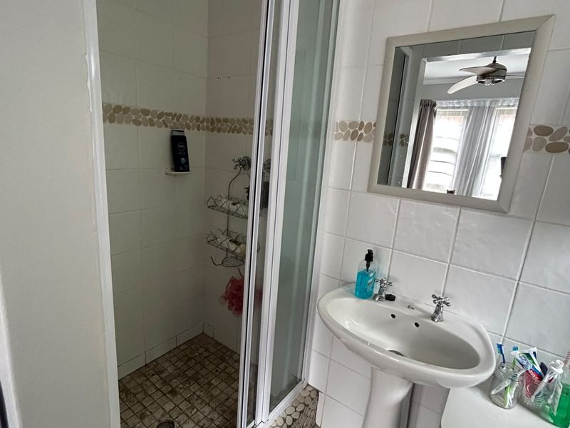 A functional bathroom featuring a pedestal basin, a shower enclosure with tiled finishes, and wall-mounted mirror.