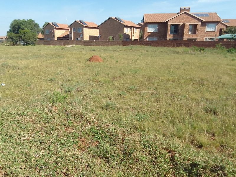 A view of a vacant residential plot of land with established grass, situated in a developed neighborhood.