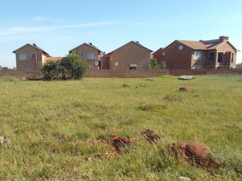 A vacant residential plot of land featuring natural grass cover and enclosed by a perimeter brick wall, situated in a developed residential area.