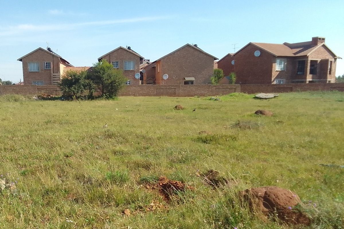 A vacant residential plot of land featuring natural grass cover and enclosed by a perimeter brick wall, situated in a developed residential area.