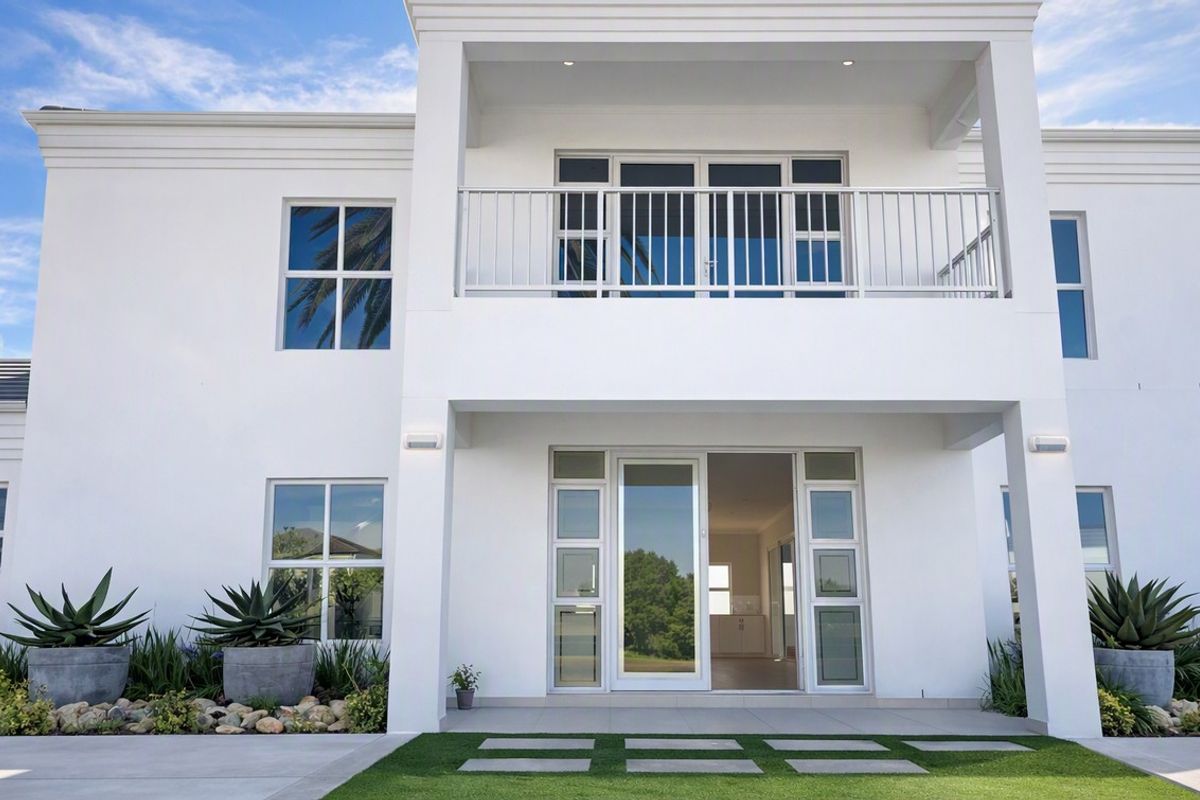 Modern two-story rear facade featuring a covered ground-floor patio, an upper-level balcony with metal railing, and large glass sliding doors.