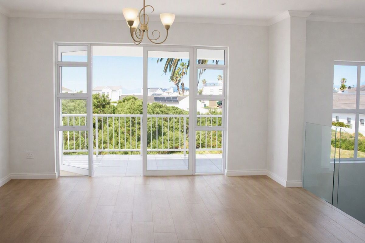 Bright and spacious living area featuring light laminate flooring, modern glass balustrade, and large sliding doors opening onto a balcony with scenic views.