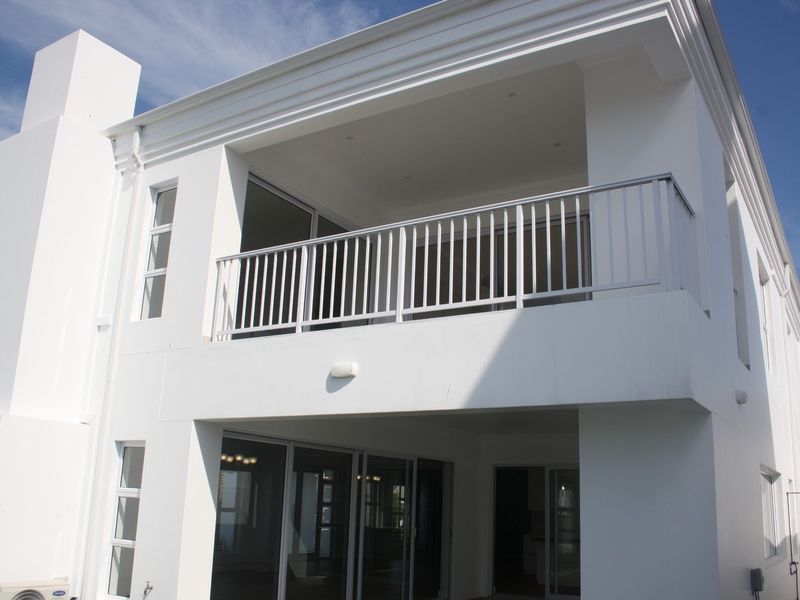 A modern rear exterior view featuring a spacious balcony with metal railings, large sliding glass doors, and a prominent chimney structure.