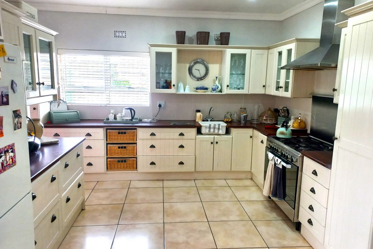 A well-maintained kitchen featuring cream-colored cabinetry, dark laminate countertops, a gas stove with an extractor fan, and ceramic tile flooring.