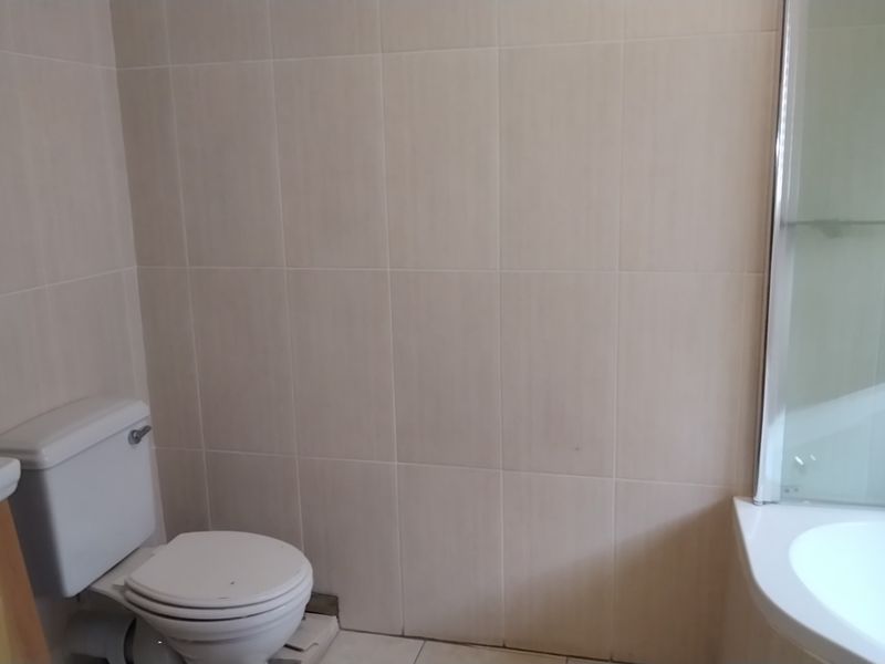 A functional bathroom featuring neutral wall tiles, a standard toilet, and a bathtub with an integrated shower screen.