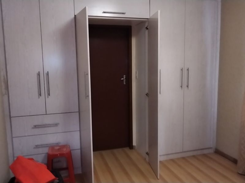 A bedroom featuring light-toned built-in cupboards with integrated storage and laminate flooring, providing a functional and neutral space.