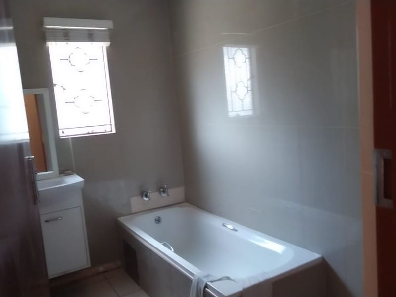 A clean, functional bathroom featuring a built-in bathtub, vanity cabinet with basin, and neutral wall tiling.