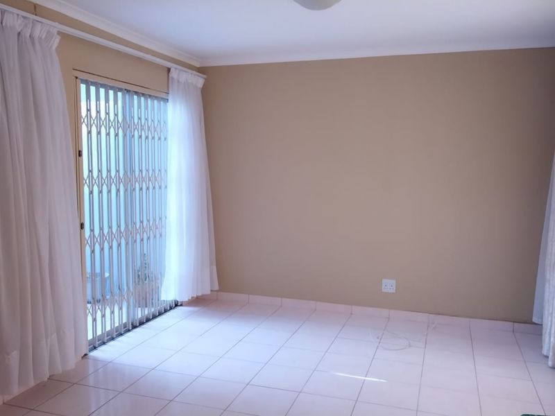 A bright, empty living area featuring neutral wall tones, tiled flooring, and a sliding glass door with a security gate leading outdoors.