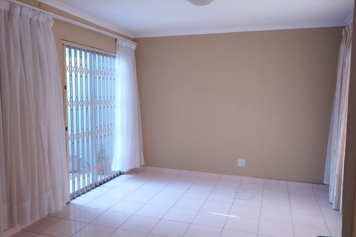 A bright, empty living area featuring neutral wall tones, tiled flooring, and a sliding glass door with a security gate leading outdoors.