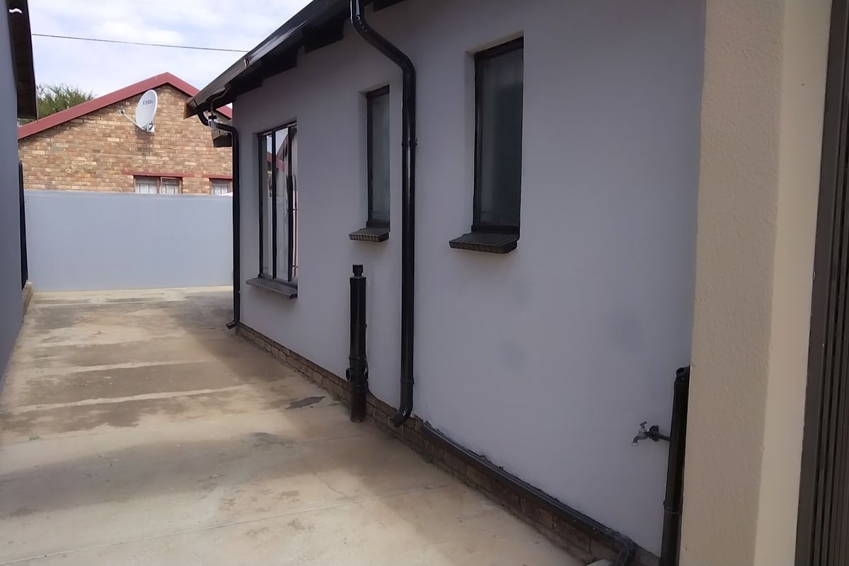 A side view of the property showing a paved walkway, boundary wall, and exterior wall finishes with downpipes and an outdoor water tap.