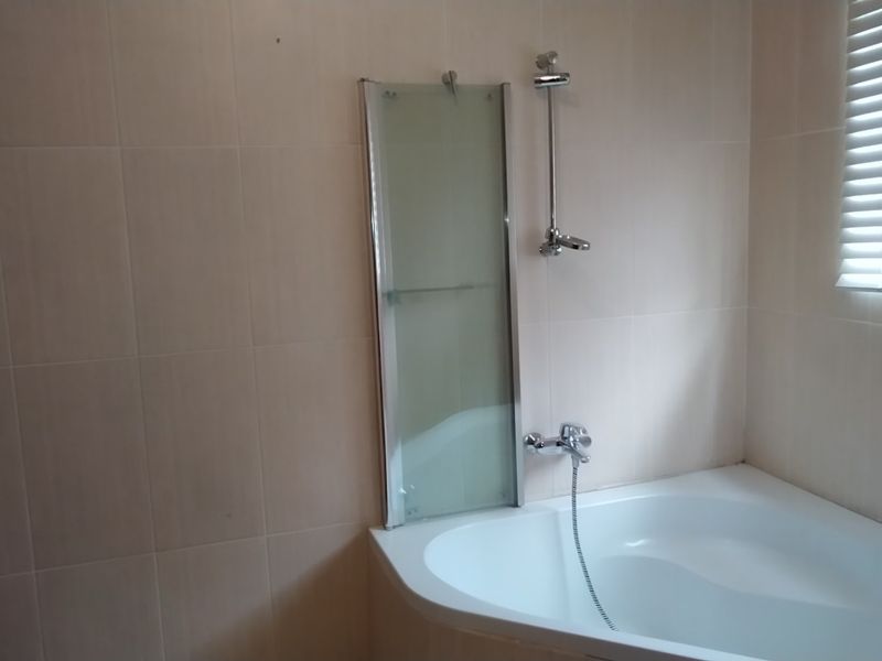A functional bathroom featuring a corner bathtub with a shower mixer, glass screen, and neutral wall tiling.