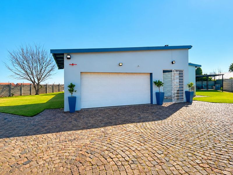 A well-maintained detached garage featuring a white sectional door, security gate, and a spacious cobblestone driveway set within a landscaped garden.