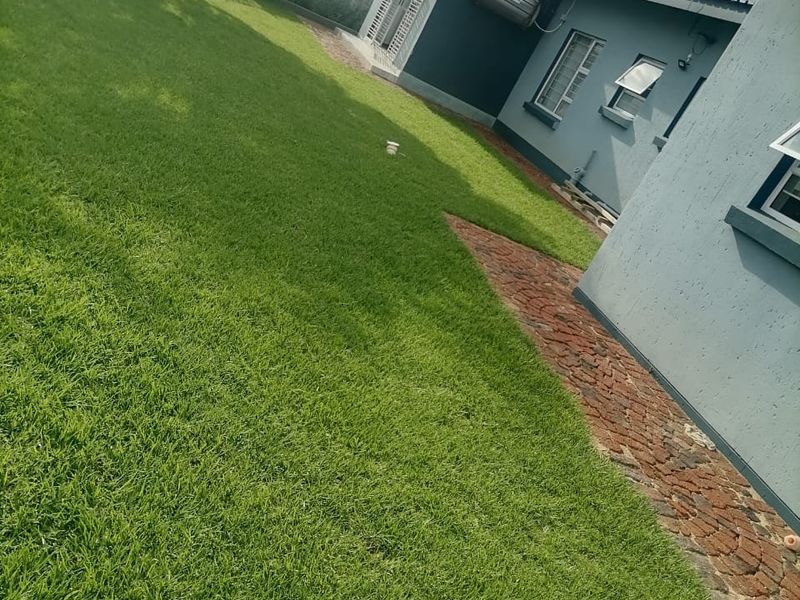 A well-maintained rear garden featuring a lush lawn, brick paved pathway, and a solar water heating system installed on the exterior wall.