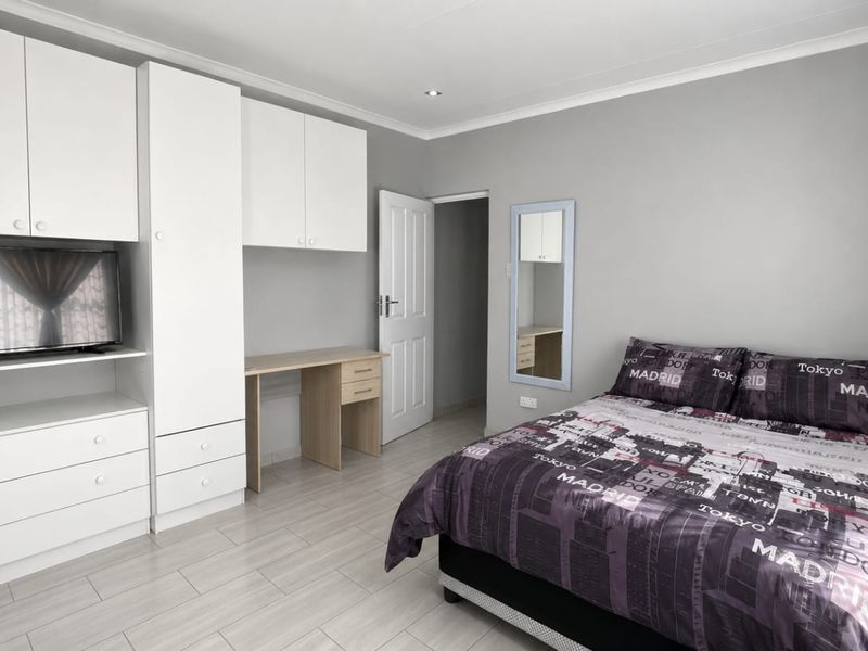 A well-maintained bedroom featuring extensive built-in cabinetry, a dedicated desk area, and neutral tiled flooring.
