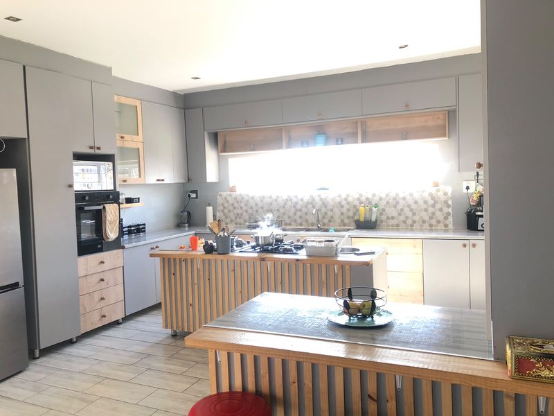 Modern kitchen featuring grey and wood-toned cabinetry, a central island with a gas hob, tiled backsplash, and integrated appliances.