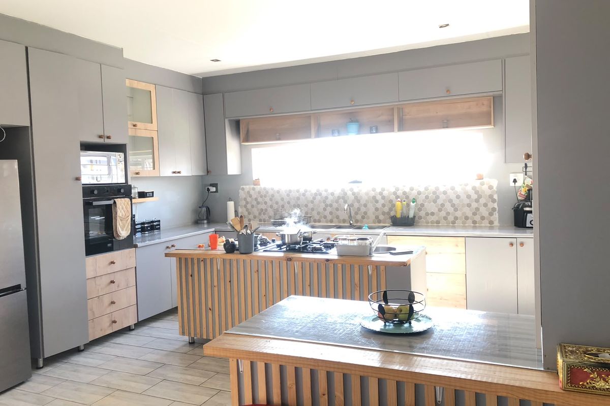Modern kitchen featuring grey and wood-toned cabinetry, a central island with a gas hob, tiled backsplash, and integrated appliances.
