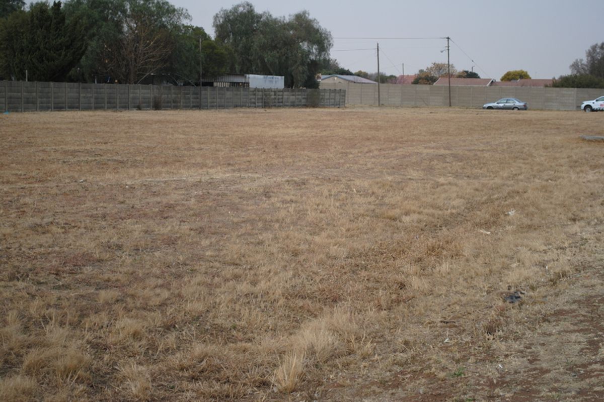 A vacant residential plot featuring dry grass, enclosed by a precast concrete boundary wall with overhead power lines visible in the background.