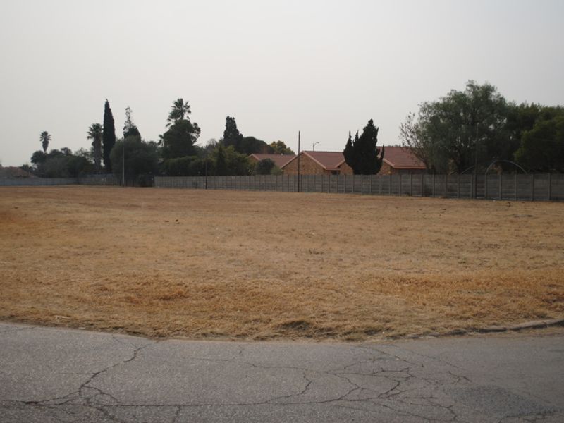 A vacant residential plot featuring a level grassed area enclosed by a precast concrete boundary wall, situated along an existing asphalt road.