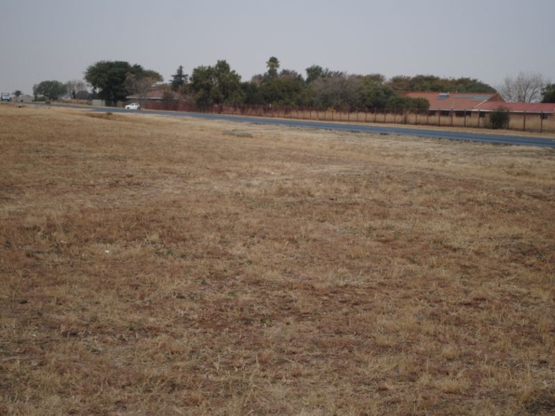 A view of the vacant residential land plot adjacent to a paved road with perimeter fencing visible in the background.