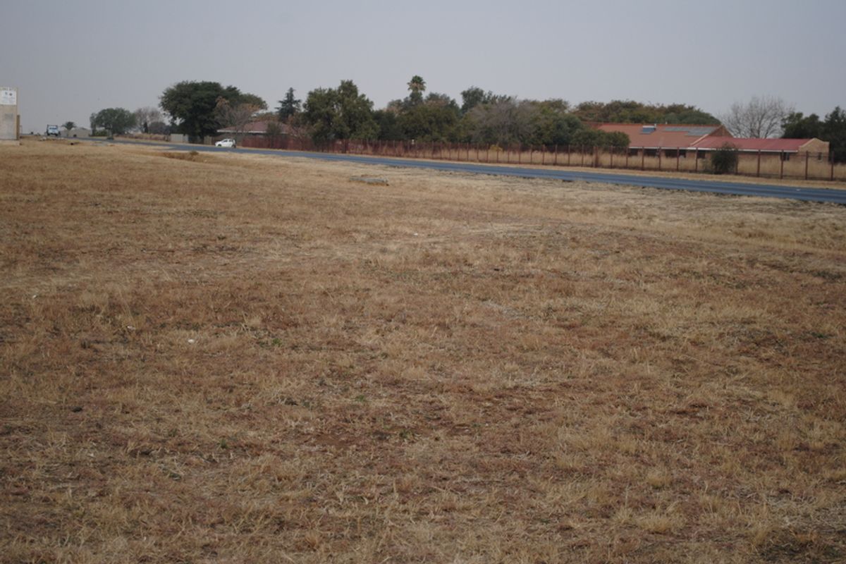 A view of the vacant residential land plot adjacent to a paved road with perimeter fencing visible in the background.