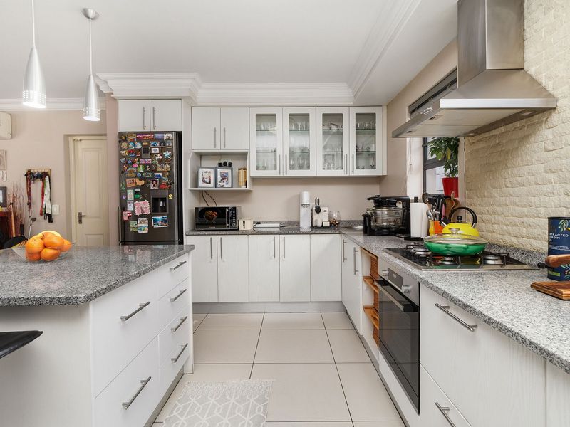 Modern kitchen featuring granite countertops, a central island, built-in oven with gas hob, extractor fan, and ample cabinetry with a stylish exposed brick accent wall.
