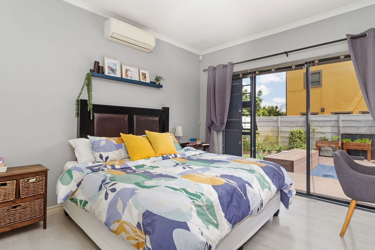 Bright bedroom featuring laminate flooring, a wall-mounted air conditioner, and large sliding glass doors providing direct access to the outdoor patio and pool area.