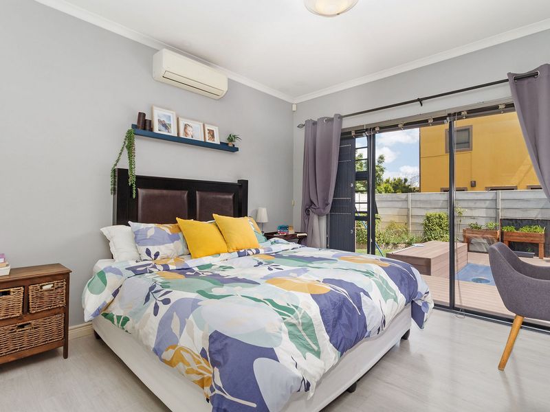 Bright bedroom featuring laminate flooring, a wall-mounted air conditioner, and large sliding glass doors providing direct access to the outdoor patio and pool area.