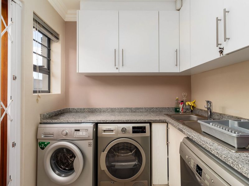 Compact laundry room featuring granite countertops, stainless steel sink, and ample built-in cabinetry for organized storage and utility use.