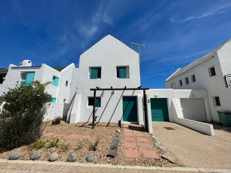 Front elevation of a white-painted house featuring a garage, a wooden pergola over the entrance, and a low-maintenance gravel garden with paved path.