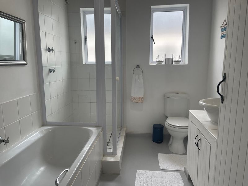 A functional bathroom featuring a built-in bathtub, separate glass shower enclosure, toilet, and a vanity cabinet with a vessel sink.
