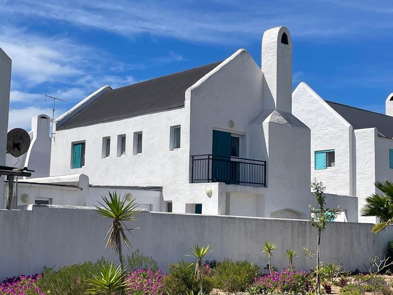 A well-maintained white house featuring a prominent chimney, a small balcony with metal railings, and traditional shuttered windows, set behind a low boundary wall.
