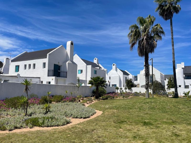 A view of the rear exterior of the white residential complex featuring landscaped gardens, manicured lawns, and distinct architectural chimneys.