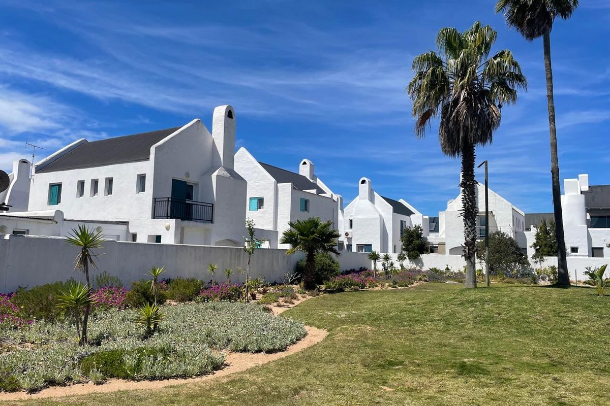A view of the rear exterior of the white residential complex featuring landscaped gardens, manicured lawns, and distinct architectural chimneys.