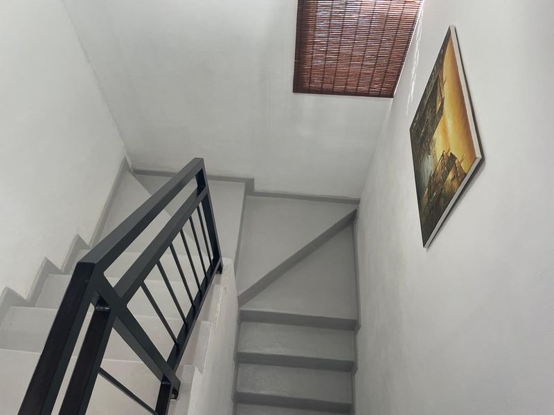A clean, minimalist staircase featuring grey painted steps and a modern black metal balustrade, illuminated by a ceiling skylight.