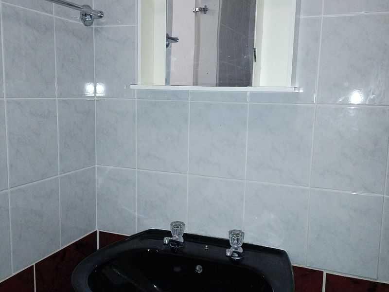 A functional bathroom vanity area featuring a black basin, chrome faucets, and a wall-mounted mirror cabinet against tiled walls.