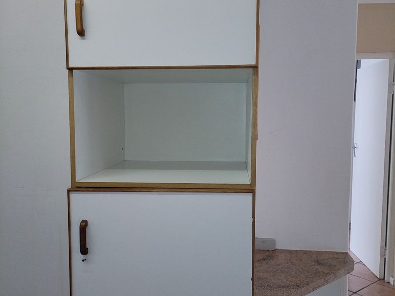 A close-up view of built-in kitchen cabinetry featuring white doors with wooden trim and a stone countertop surface.