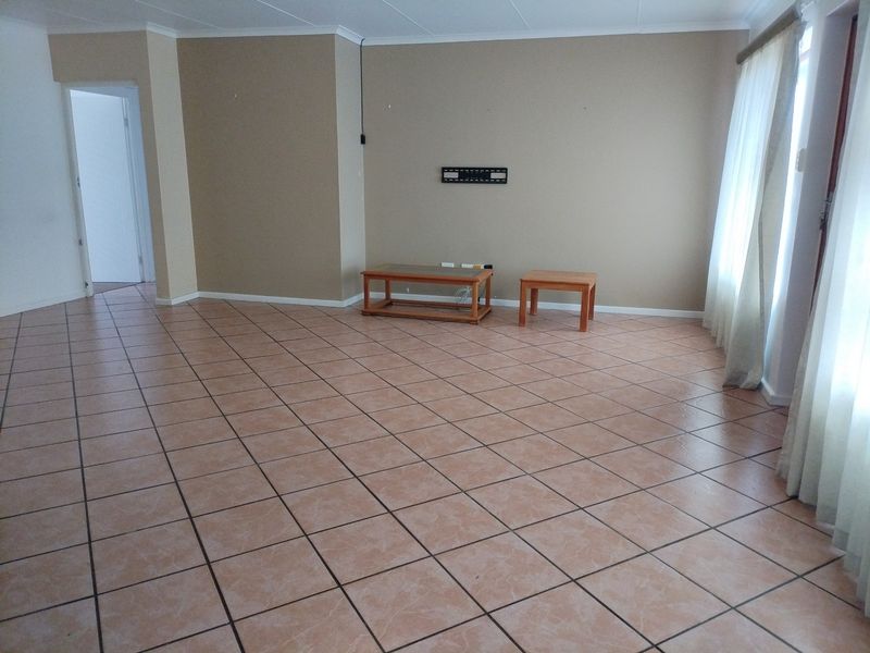 Spacious living area featuring neutral wall tones, tiled flooring, and a wall-mounted television bracket, offering a clean and versatile space for customization.