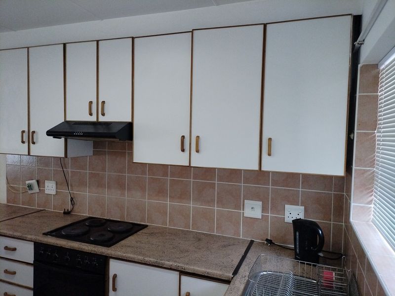 A functional kitchen featuring white built-in cabinetry, a laminate countertop, an electric hob with extractor fan, and a tiled backsplash.