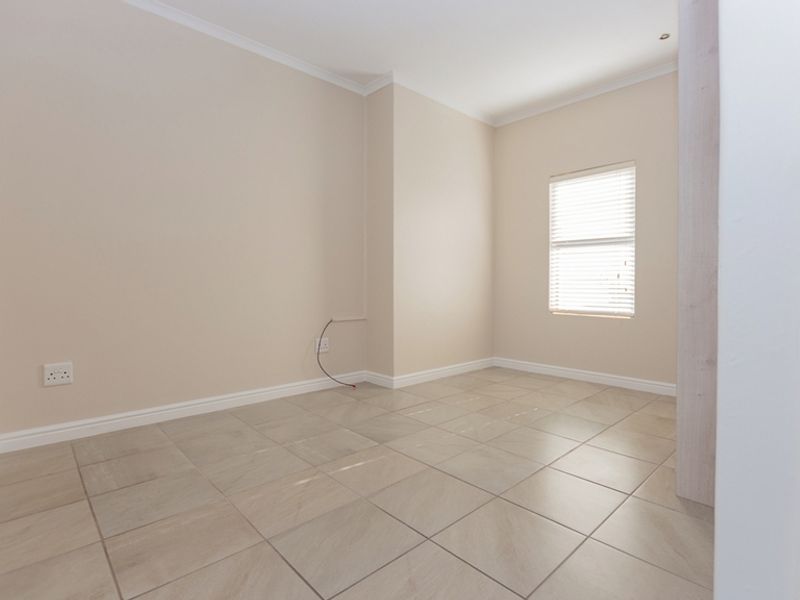 A bright, empty bedroom featuring neutral tiled flooring, clean walls, and fitted venetian blinds, offering a blank canvas for personalization.
