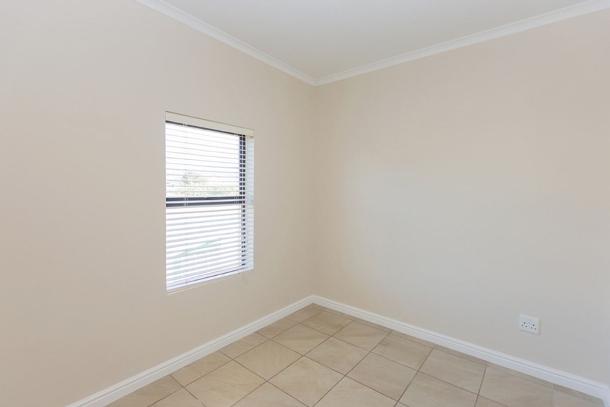 A clean, empty bedroom featuring neutral wall paint, tiled flooring, and a window fitted with venetian blinds.