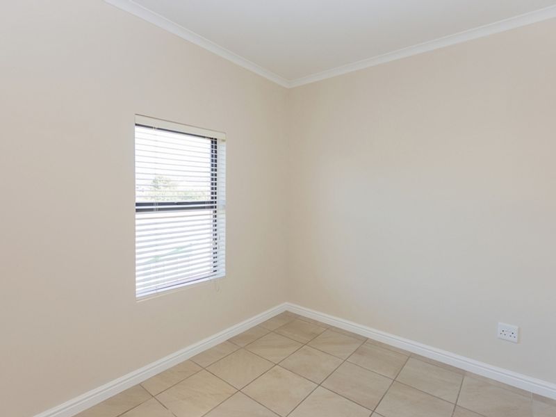A clean, empty bedroom featuring neutral wall paint, tiled flooring, and a window fitted with venetian blinds.