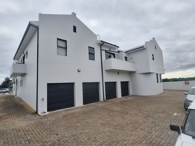 Rear view of the apartment complex featuring four garage doors, a paved driveway, and upper-level balcony access.