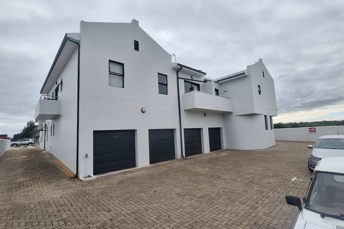 Rear view of the apartment complex featuring four garage doors, a paved driveway, and upper-level balcony access.